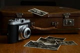 Vintage suitcase with camera and scattered black and white photographs