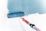 A paint roller applying blue paint to a white wall.