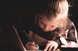 A young girl poised with a pen over a notebook, presumably completing her homework