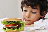 A boy looks longingly at a burger, he slicks his lips, ready to eat, I have had the burger, Tim’s Grateful 8