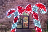 2 giant candy canes with a giant bow in the middle made from fairy lights outside the entrance to a building