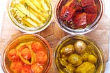 four jars of oil and confit’d veg — parsnip, beet, tomato, and potatoes — in rich color