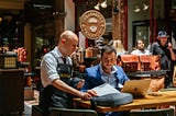 Small-business owner reviews documents with a retail associate while working on a laptop in a shop setting. Photo by Johan Mouchet on Unsplash