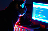 A cat coding in a dark room with headphones and facing monitor