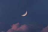 a quarter moon in the middle of a dark blue night sky with pink clouds puffing down below