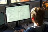 developer sitting at a computer desk looking at a screen wearing blue hoodie