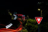 A photo at night of a yield sign near a busy highway.