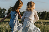 two little girls running in a field of grass