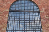 A large red brick wall with a large window with a arched top and a bicycle in front.