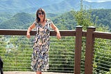 Picture of author wearing a nice dress and sunglasses in front a a spectacular view of the smokey mountains. Subject looks fancy because she is at a wedding — she looks confident with a slight smile and attitude.