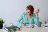 Image showing a woman executive with crumpled papers on desk, trying to write the perfect note.