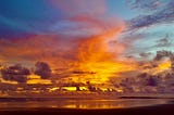 A dazzling display of sunset colours fills a cloudy coastal sky