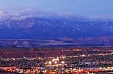 The metropolitan area of St. George, Utah (population 208,000 in 2024). The cloud-covered Pine Valley Mountains are in the background and low-rise buildings in the foreground. Photo by St. George Chamber of Commerce on Wikipedia here.