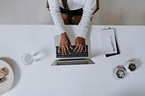 woman in white long sleeve shirt using a Macbook pro on a white desk