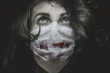 Image of a woman wearing a surgical mask with blood stains on it.
