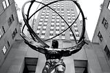 A bronze statue of Atlas holding the world — placed somewhere in NewYork — amongst skyscrapers