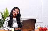 A female UX Designer wearing reading glasses and smiling at her computer