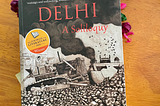 Image of the book, Delhi: A Soliloquy by M Mukundan lying on the table with dried flowers and another book, City of Djinns by William Dalrymple.