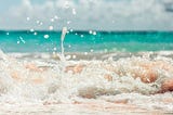 white foam ocean waves wash over pink sand beach