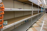 A grocery store aisle showing empty shelves where toilet paper should be.