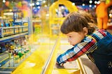 Young child looks longingly at Lego display behind glass.