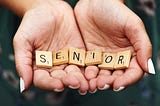 Macro shot of teen girl with manicured fingernails holding scrabble letters spelling the word “SENIOR” in the palms of her cupped hands.