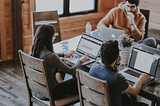 3 people sitting at a table in front of laptops