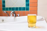 A glass of beer placed on a surface near a running tap.