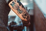 Tattoos on the back of an arm. The words “hard work” appear on a hammer with a skull underneath.
