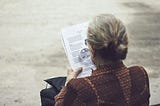 Woman reading from a sheet of paper with a magnifying glass.