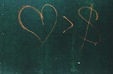 Graffiti on a wall showing a heart in preference to a dollar sign.