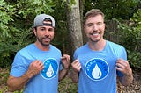 MrBeast and another supporter stand outdoors in matching light blue #TeamWater shirts, smiling and pointing at the campaign logo to promote global access to clean drinking water.