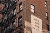 Picture of a brick building with a sign that says ‘How are you, really?’