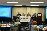 A group of four panelists presenting to a room of higher education professionals.