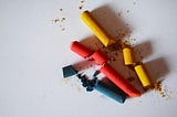 three broken crayons of colors yellow, red and navy blue laying next to one another on a white surface