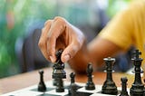 A person’s hand moves a chess piece across a chess board