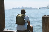 A man sitting on a bench wearing the MTW Backpack looking at San Francisco.