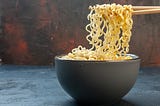 A bowl of instant noodles with a pair of chopsticks holding some of them on the bowl.