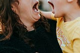 Mom holding young sons. Their facial expressions look like they’re playfully yelling.