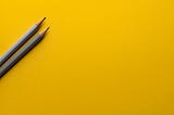 Two pencils on a yellow surface.