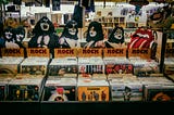 Rock album bins at used vinyl record store. Images of members of KISS and the Rolling Stones’ “mouth and extended tongue” logo displayed above.
