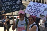 Man and woman with pink hats holding signs.