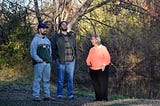 Three people stand in the woods