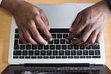 A picture of two hands, typing on a laptop computer.