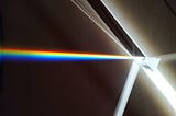 a glass prism with a narrow beam of light being refracted into a rainbow