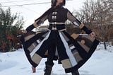 A woman in a sweater coat of brown, white and black, posing in a snowy backyard setting.