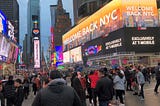 A crowded Times Square in New York, with a digital billboard that reads, “WELCOME BACK NYC”