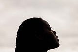 A Black woman looks up pensively in a white background.