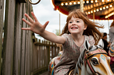 Girl on old fashioned wood carousel reaching for the gold ring prize