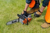 A man bending over to pick up a chainsaw.